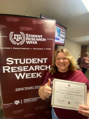 Image of Rachelle Pederson giving thumbs up with award in front of SRW sign